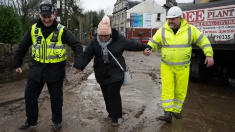 Getty Images A woman helped through mud in Mountain Ash, Rhondda Cynon Taf, by a police officer and a council worker