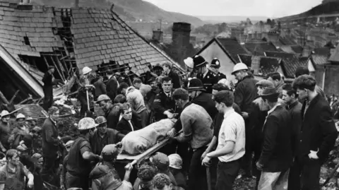 Getty Images Black and white photo of emergency workers carrying out a body on a stretcher 