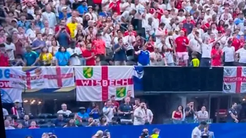 Inside a football stadium where a Wisbech St George Cross flag can be seen amongst the England fans.