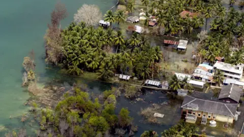 Getty Images Pemandangan udara dari Helikopter Angkatan Laut India yang diambil pada 28 Februari 2005, menunjukkan sebuah desa pesisir tergenang air yang terbengkalai di Pulau Kamorta, bagian dari Kepulauan Andaman dan Nikobar. India sudah putus asa untuk membangun kembali enam pulau di kepulauan Andaman dan Nikobar yang dilanda tsunami, dimana 5.764 orang masih terdaftar sebagai orang hilang dan sekitar 40.500 orang ditempatkan di kamp-kamp sementara menunggu rumah mereka dibangun kembali oleh Komando Bantuan Terpadu (IRC). , terdiri dari pemerintahan militer dan sipil, yang dibentuk oleh India untuk memulihkan Kepulauan Andaman. 