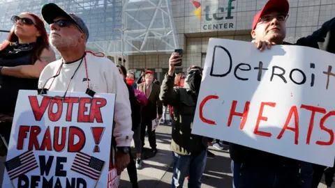 Getty Images Two male protesters in Michigan hold signs claiming voter fraud. One reads "Voter fraud" and other other "Detroit cheats".