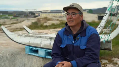 BBC Kaleeraq Mathaeussen sits in front of an old wooden dog sled