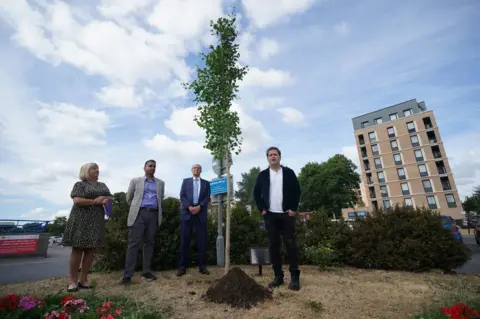 PA Media Doctor and best-selling author Adam Kay (right), who wrote BBC hospital drama This Is Going To Hurt, plants a tree at Ealing Hospital,