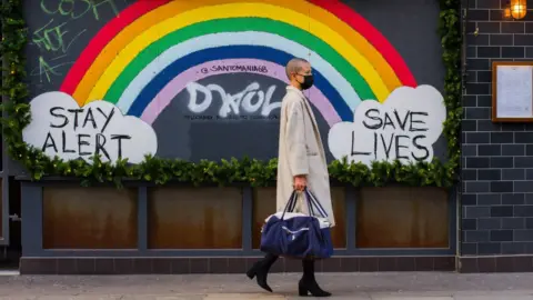 Getty Images Woman walks past a "stay alert" sign