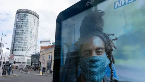 Getty Images man with locs wearing face-mask on NHS poster