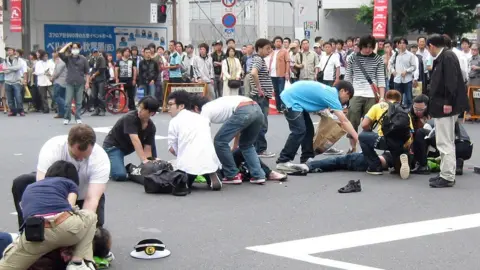 STR/AFP via Getty Images People attend injured victims lying on the road after they stabbed in the attack at Tokyo's Akihabara electronics shops district on June 8, 2008