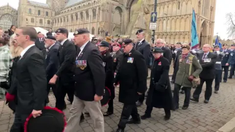 Veterans, many with medals and wearing berets, march past the Cathedral