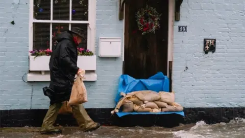 PA Media A man places sand bags outside a property in Langstone, Hampshire