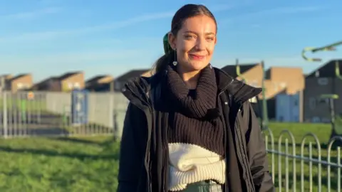 Woman with long dark hair wearing a black raincoat in a housing estate