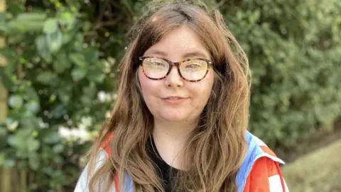 Martin Giles/BBC Young woman sitting on a park bench in Norwich