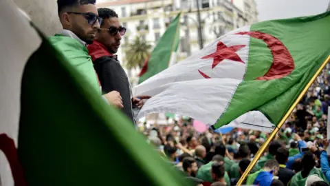 Getty Images Algerian protesters wave a national flag as they take part in a demonstration in the capital Algiers on May 3, 2019. - Algerians gathered for an 11th consecutive Friday of demonstrations.