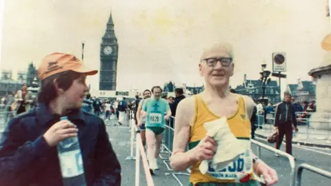 Roger Markham An old photo of a 78 year old marathon runner with a youth running alongside handing him water. The Big Ben clock tower is in the background. 