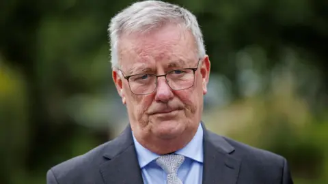 PA Media Mike Nesbitt in grey suit, blue shirt and grey patterned tie. He is outside. He has grey hair and glasses.