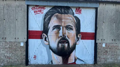A picture of Harry Kane's face, with a St George's flag as the background, on a big corrugated metal door.
