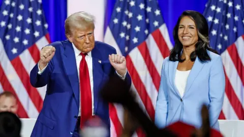 Getty Images Donald Trump dancing on stage with his director of national intelligence Tulsi Gabbard smiling. Both have US flags behind them