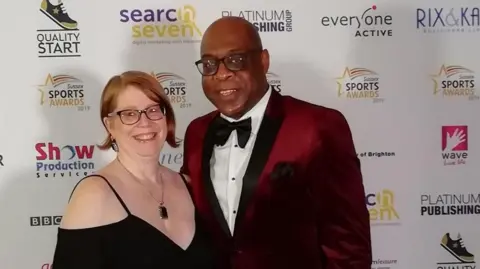 Eric and Mandi Douglin pose before a sponsor board at an awards event. Both are wearing formal attire.