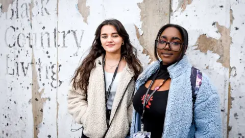 Friends in the street outside a decaying wall that reads Black Country Living