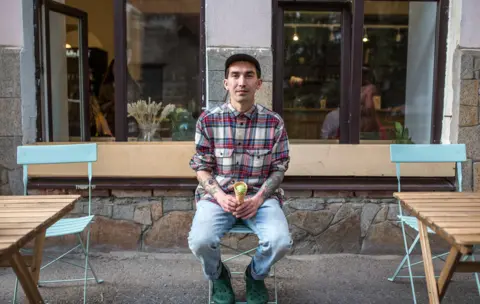 BBC Slava sitting outside his cafe, Fika, holding a green matcha flavoured ice cream in a cone