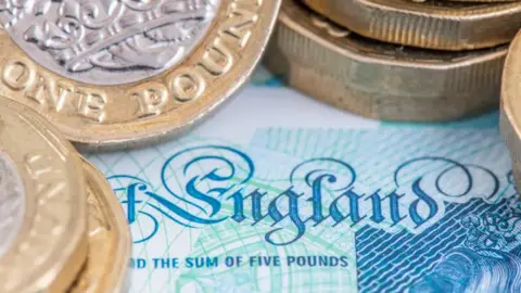 Coins are positioned on a £5 note