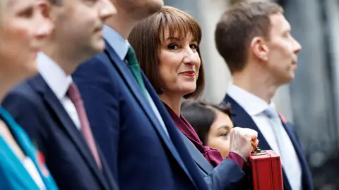 EPA Rachel Reeves poses for the cameras with a line up of her Treasury ministers. She is smiling and holding the traditional Budget red box