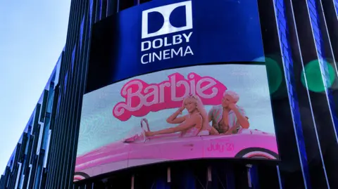 Getty Images A TV screen poster of the film Barbie on the outside of the Odeon Cinema building in Leicester Square. It features Margot Robbie, driving a pink car and Ryan Gosling in the back seat.