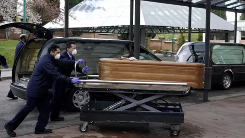 Reuters Employees of a mortuary enter the crematorium of La Almudena cemetery with a coffin of a person who died of coronavirus disease in Madrid, March 23, 2020