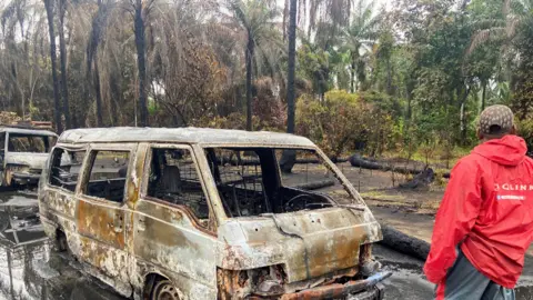 Reuters A man near burn-out vehicles after an explosion at an illegal oil refinery in the Niger Delta, Nigeria - April 2022