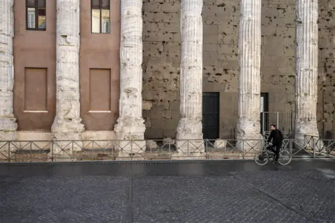 EPA A man rides a bike past ancient stone columns