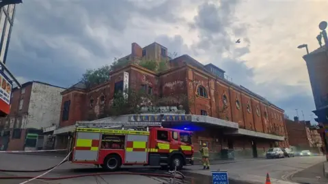 A fire engine parked by a crumbling theatre site