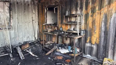 Fire damaged room. The room is black and charred. A worktop is badly damaged. Melted items are scattered on the floor.