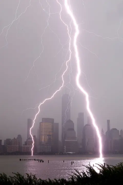 Gary Hershorn/Getty Images Lightning bolts hit a river with a city skyline behind