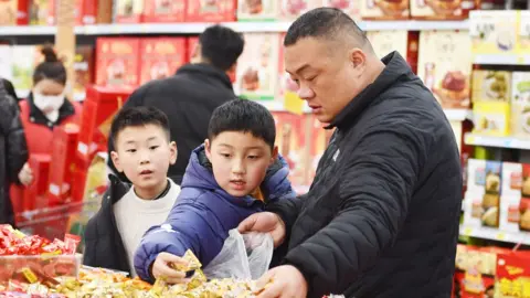 Getty Images A man and his two children choosing sweets in a supermarket.