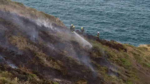 Sue Daly A fire crew hoses down gorse on Sark's cliffs