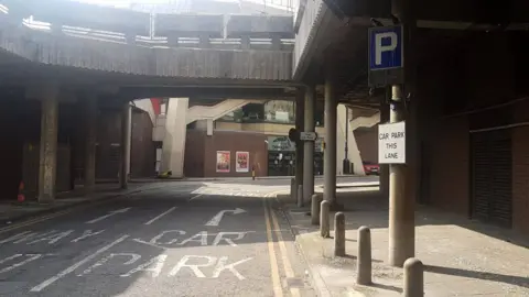 The entrance to the Broad Street Mall car park in Reading, with a blue sign with a white P in it on the right side and a sign that says "car park this lane" and directions on the road.