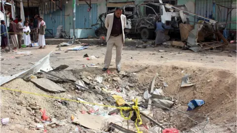 AFP A Yemeni man stands beside the crater left by a Saudi-led coalition air strike on Dahyan, Yemen (10 August 2018)