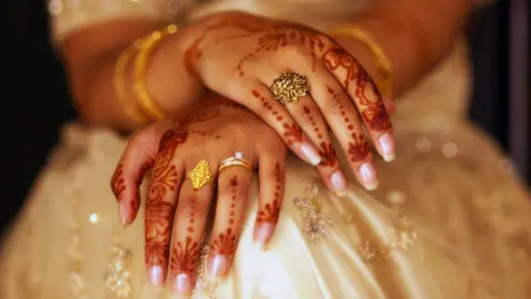 Getty Images A bride is sitting with her hand covered in henna