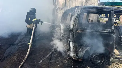 Firefighter trains hose on burnt-out vehicle in Kharkiv region of Ukraine on 7 May following Russian drone strike