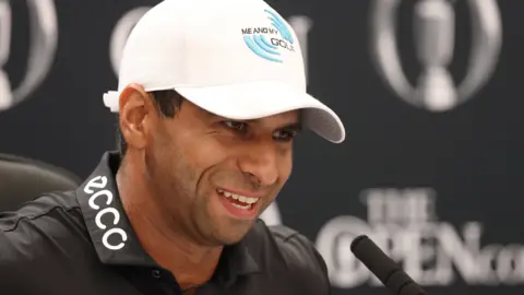 A man with a black polo shirt and white cap in front of a blurred black and white background