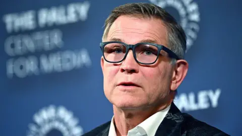 Getty Images Man with grey and black hair in glasses and in a suit with leaf patterns has his mouth slightly open as he looks towards the camera