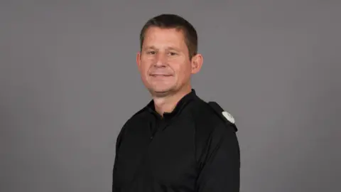 Northamptonshire Police Ivan Balhatchet with short dark hair wearing a black police shirt