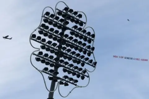 Getty Images A plane flying over a cricket pitch with a banner saying "India stop genocide & free Kashmir"