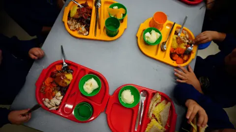 PA Media Two red and two yellow school dinner trays on a table, shown from above. The hands of the children can be seen as they tuck into their meals.