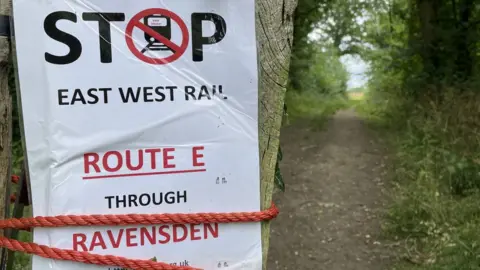 Ben Schofield/BBC A Stop East West Rail poster in Ravensden, Bedfordshire