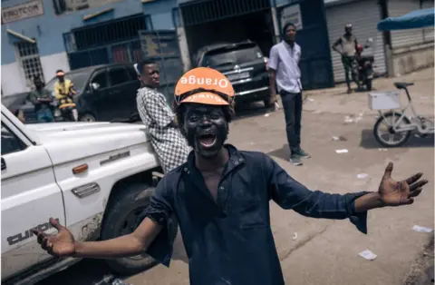 AFP A man smiling widely with his arms stretched out wide. he is wearing an orange hat.