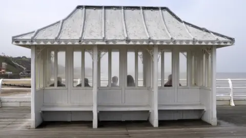 Getty Images People sitting in a weather shelter on Cromer Pier, Norfolk