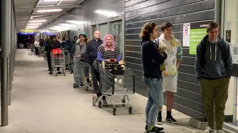 Getty Images Shoppers wait to enter a supermarket in the suburb of Johnsonville in Wellington