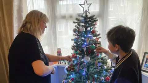 Martin Heath/BBC Mother and son standing either side of a Christmas tree and hanging decorations on it