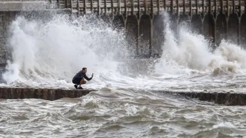 Steve Parsons/PA Media A man takes a photograph of the waves in Dawlish, Devon as gusts of up to 70mph could hit coastal areas as Storm Ellen moves on