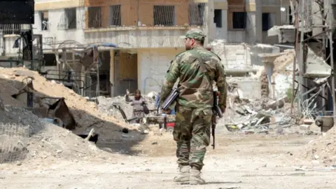EPA Syrian soldiers walk amongst destruction in the countryside of Damascus, Syria in 2018