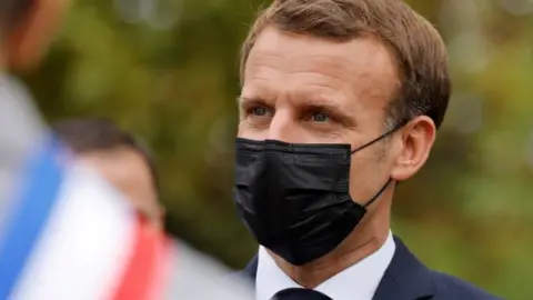 AFP French President Emmanuel Macron wearing a protective face mask speaks arriving at "la Maison des habitants" (MDH) to meet and have lunch with young representatives of the MDH in Les Mureaux, outside Paris, 2 October 2020